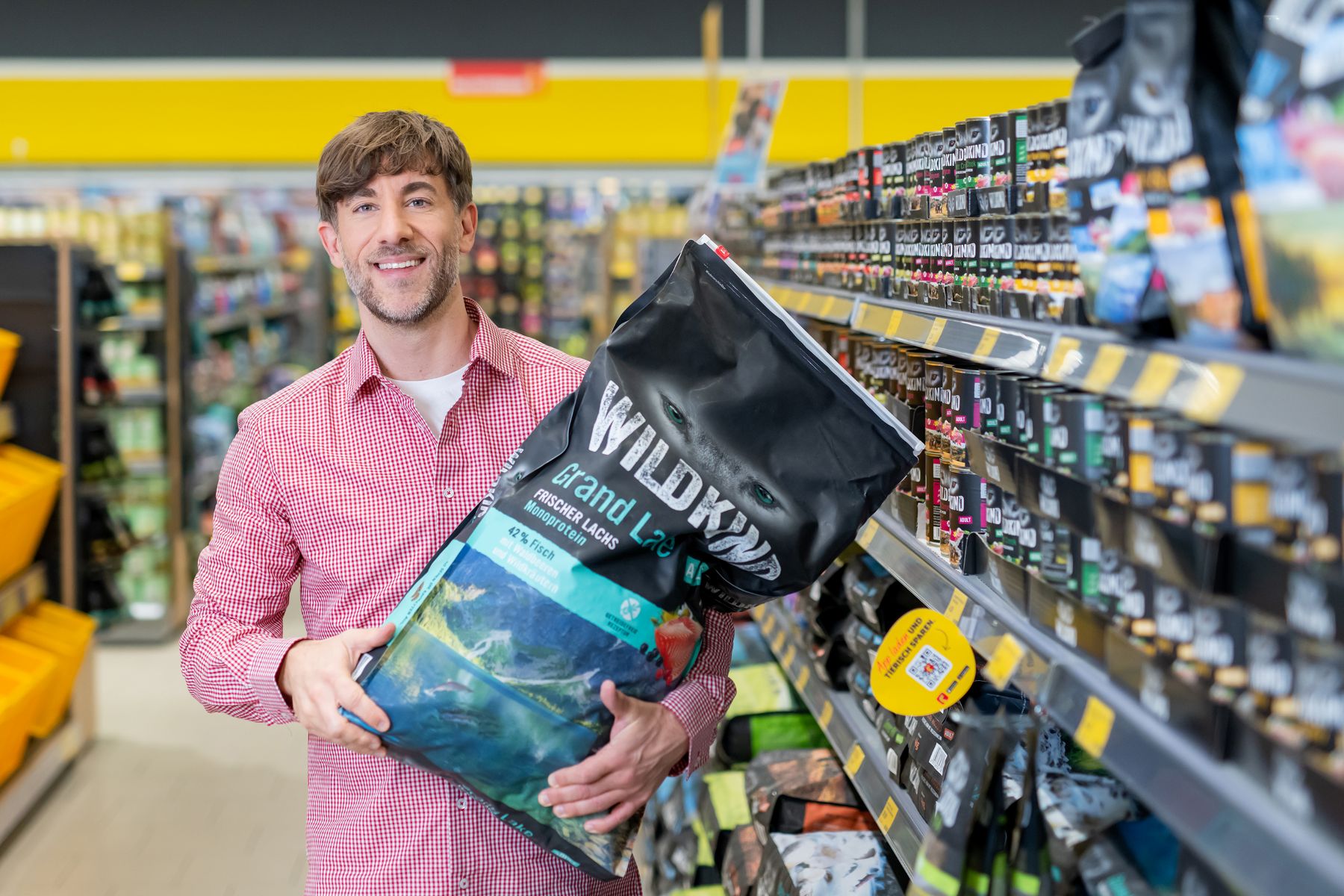 Fachberatung im FUTTERHAUS: Produktempfehlung eines Marktmitarbeitenden mit einem Sack WILDKIND Trockenfutter Grand Lake