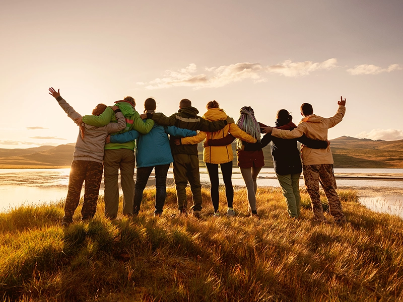 Menschen stehen Arm in Arm nebeneinander am Wasser und gucken zum Sonnenuntergang